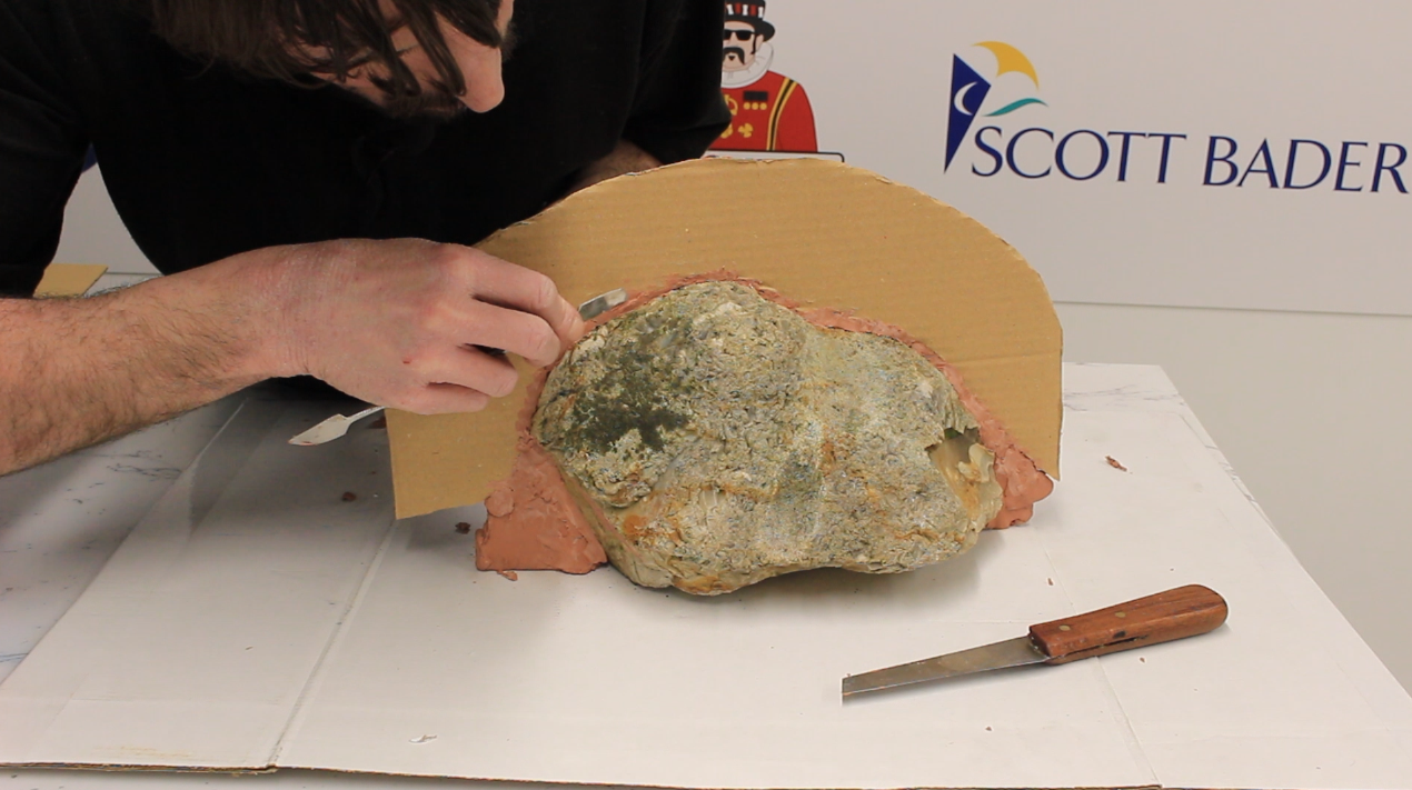 Using an oil-based clay to fill any gaps between the cardboard and rock.
